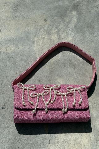 A black rectangular beaded handbag with a single strap, decorated with embroidered green olives on toothpicks, is displayed against a draped white fabric background.