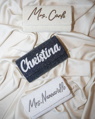 Three folded towels on cream-colored fabric. The top towel is white and embroidered with “Mrs. Carlo,” the middle is dark with “Cheristina,” and the bottom is white with “Mrs. Namarillo.”.