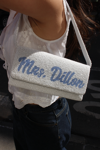 Three folded towels on cream-colored fabric. The top towel is white and embroidered with “Mrs. Carlo,” the middle is dark with “Cheristina,” and the bottom is white with “Mrs. Namarillo.”.